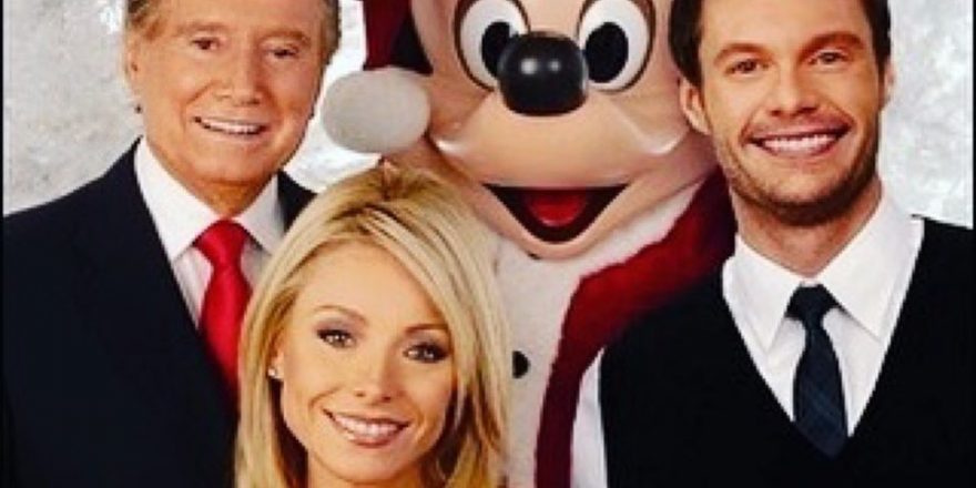Two men, a woman, and a mouse. A really big mouse. Wearing a Santa hat.