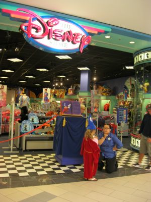Front of a Disney Store in a mall, with a kid in a costume with a staff member.