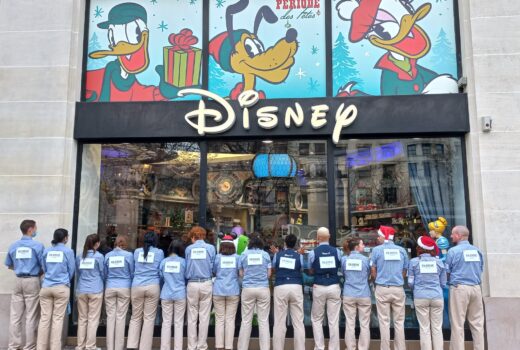 A line of Disney Store workers stand with their backs to the camera, facing into their store. They were signs saying that they are on strike.