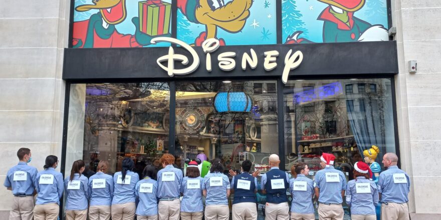 A line of Disney Store workers stand with their backs to the camera, facing into their store. They were signs saying that they are on strike.