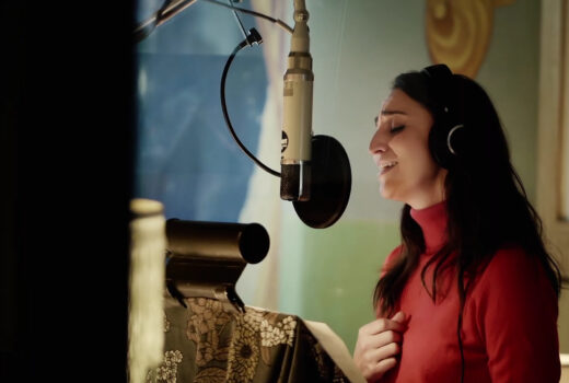 A woman, Sara Bareilles, sings into a professional microphone.