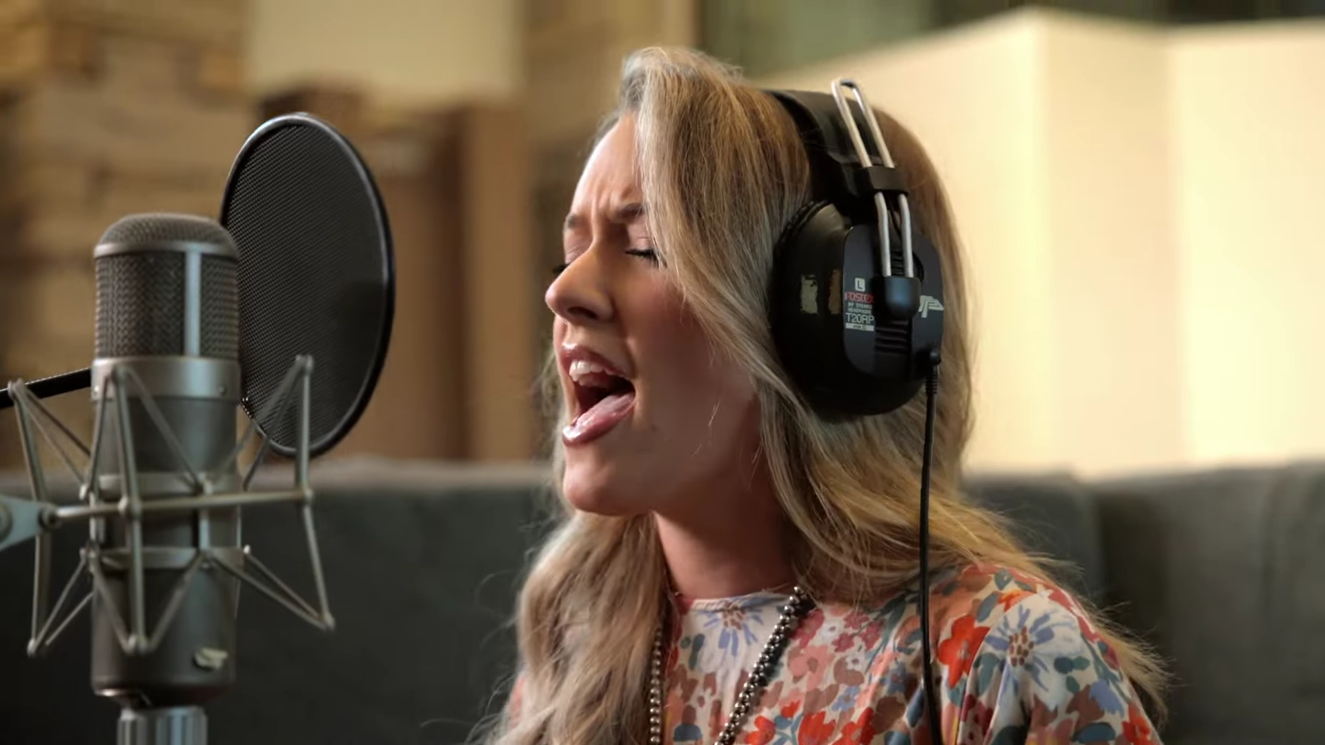 A woman belts out a song, while wearing headphones and singing into a microphone.