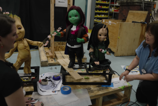 Two women work on three doll-like animatronic figures.