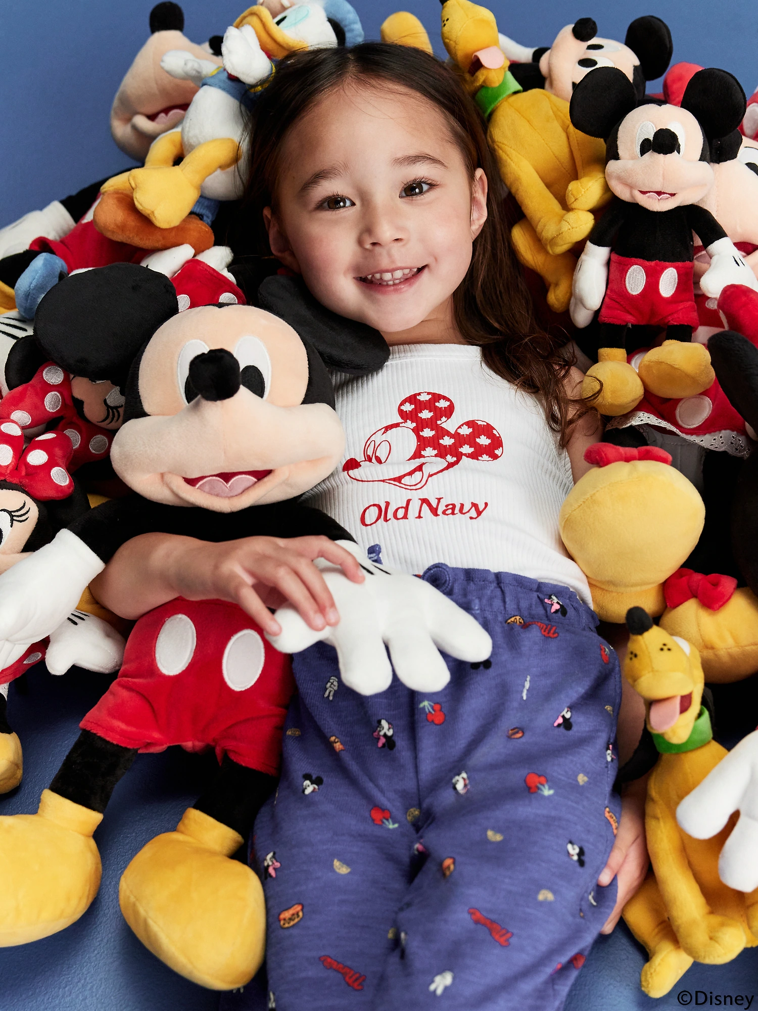 A child lays in a pile of Mickey Mouse and fab five plush toys.