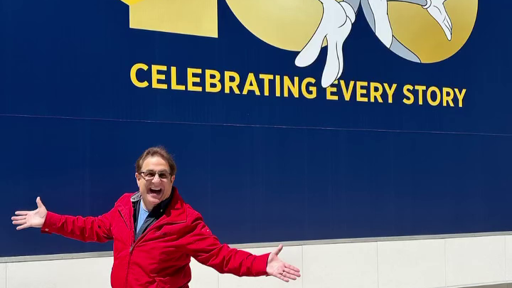 A man spreads his arms in excitement, in front of a logo with Bugs Bunny.