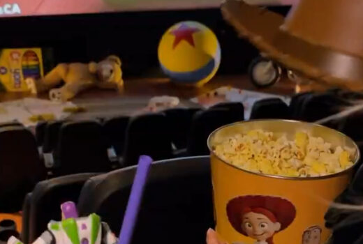 In the foreground, a popcorn bucket with a cowboy hat. In the background, items in front of a movie screen.