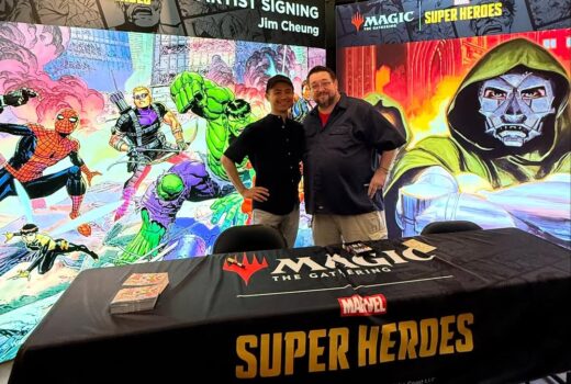 Two men at a table with comic illustrations behind them.