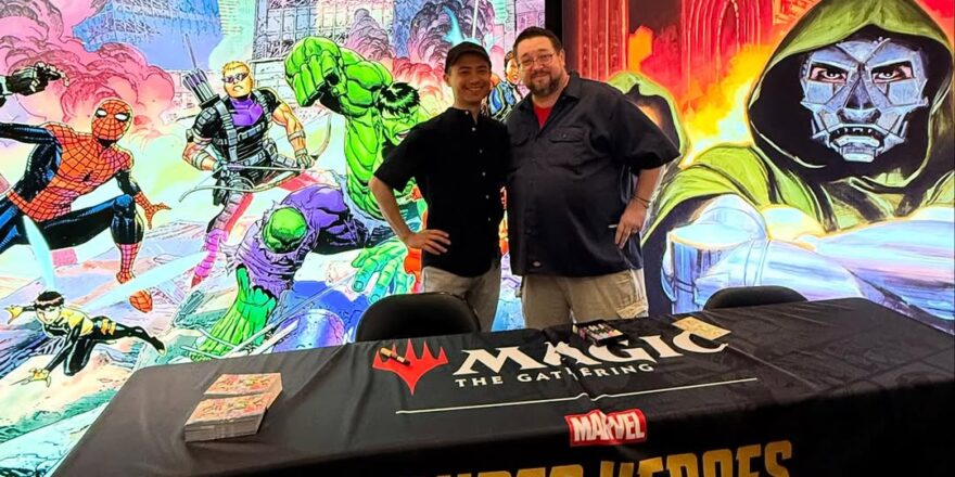 Two men at a table with comic illustrations behind them.