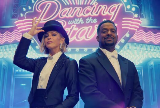A woman and man in tuxedos, in front of a neon sign.