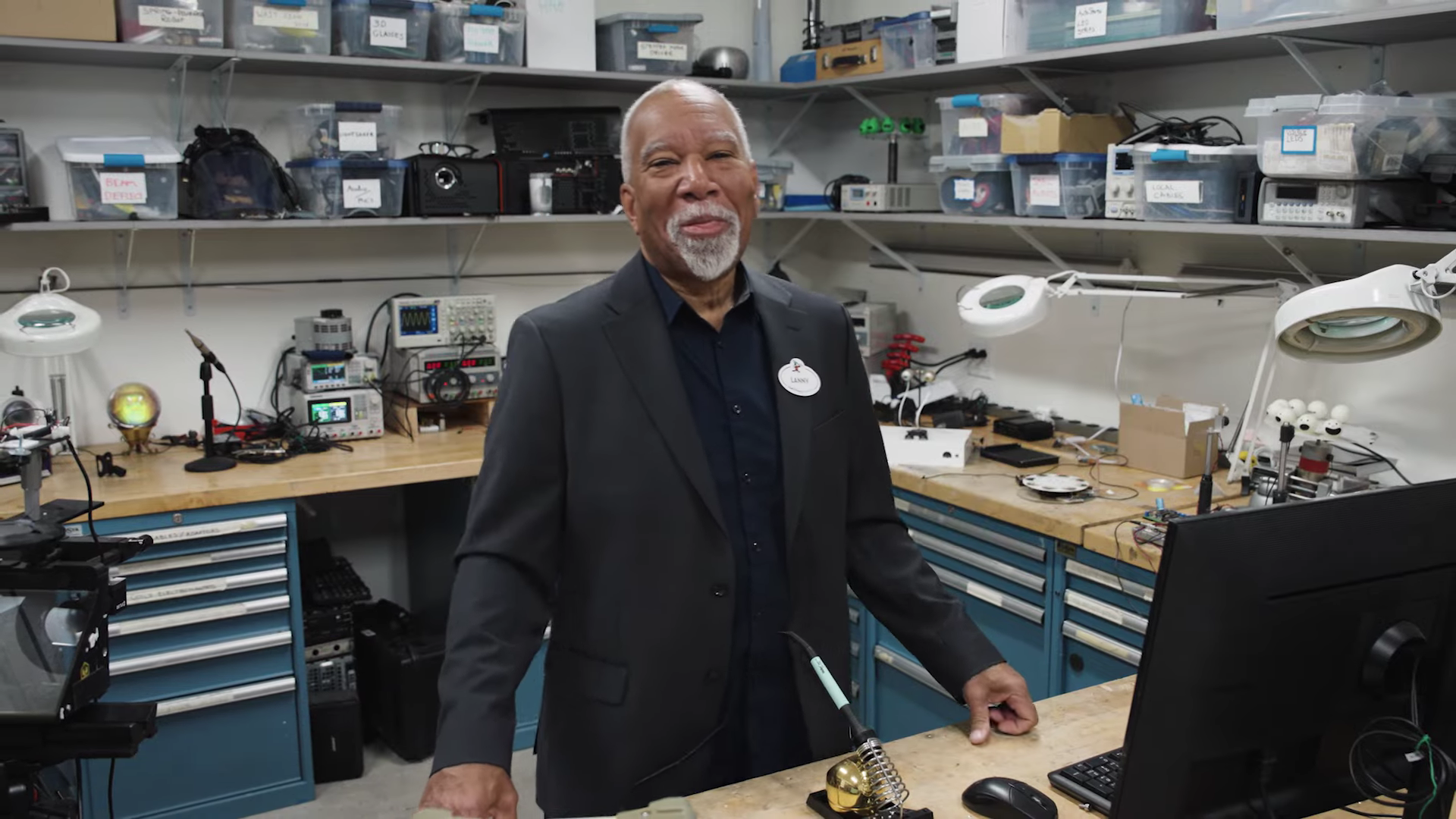 An older man poses at the desk of a workshop office.