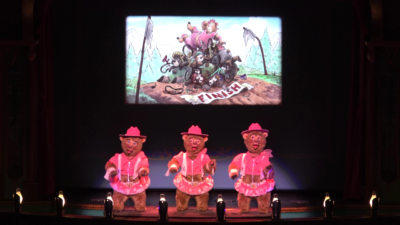 Three small female bears in front of a screen showing the mishap of a large female bear.