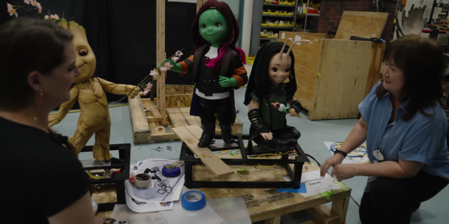 Two women work on three doll-like animatronic figures.