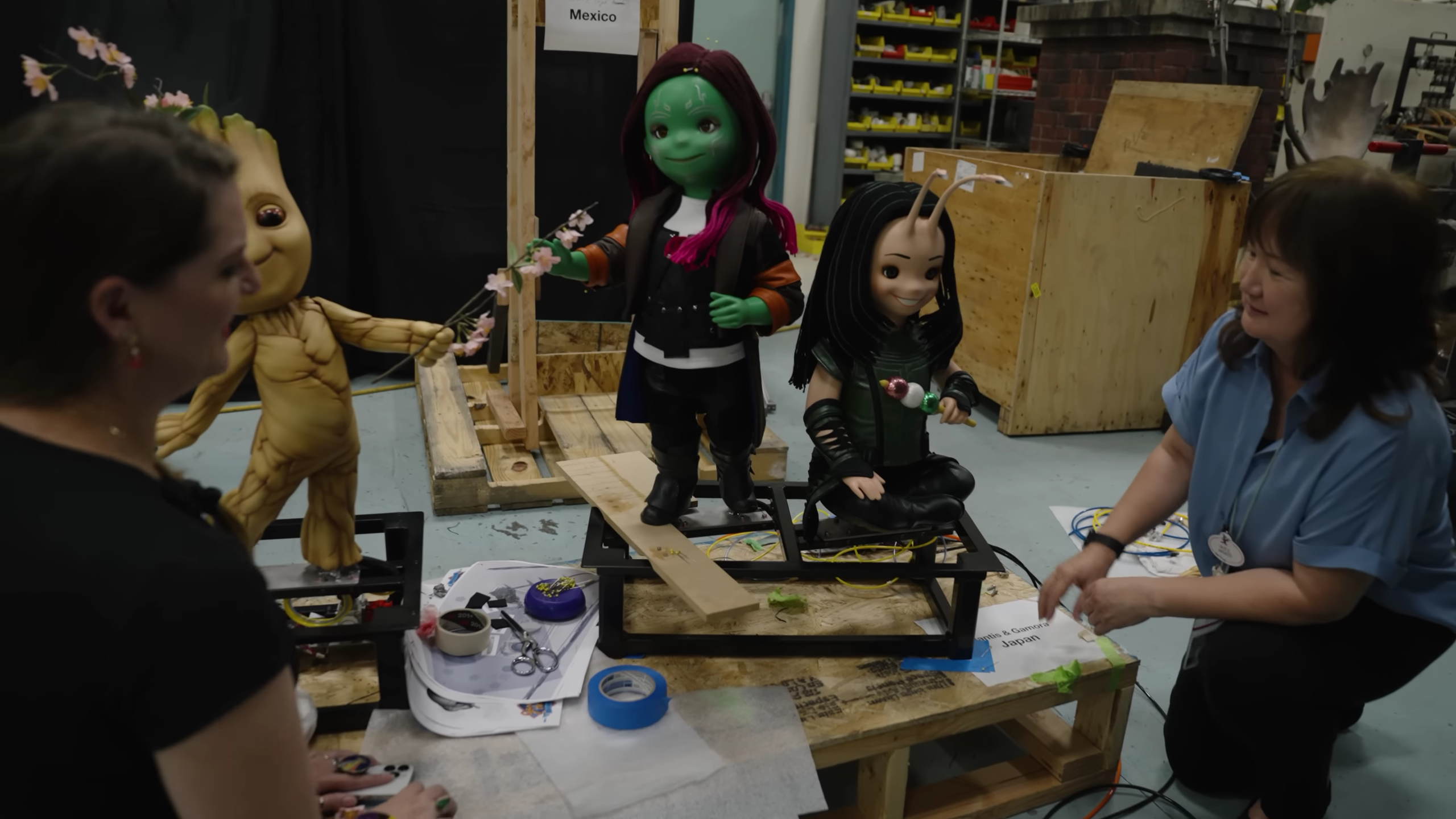 Two women work on three doll-like animatronic figures.