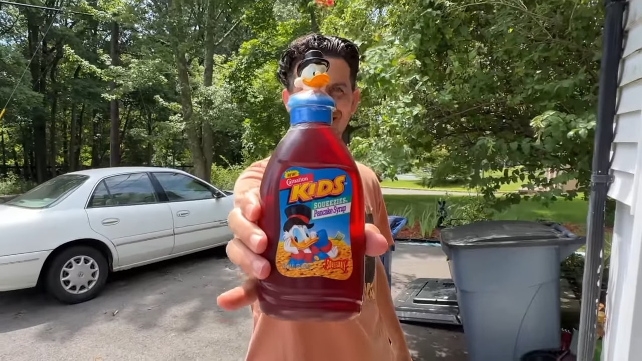 A man holds a bottle of table syrup.