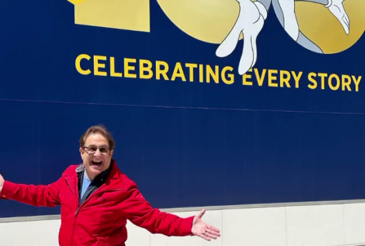 A man spreads his arms in excitement, in front of a logo with Bugs Bunny.