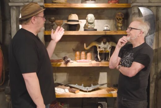 Two men in front of rustic shelves with movie props.