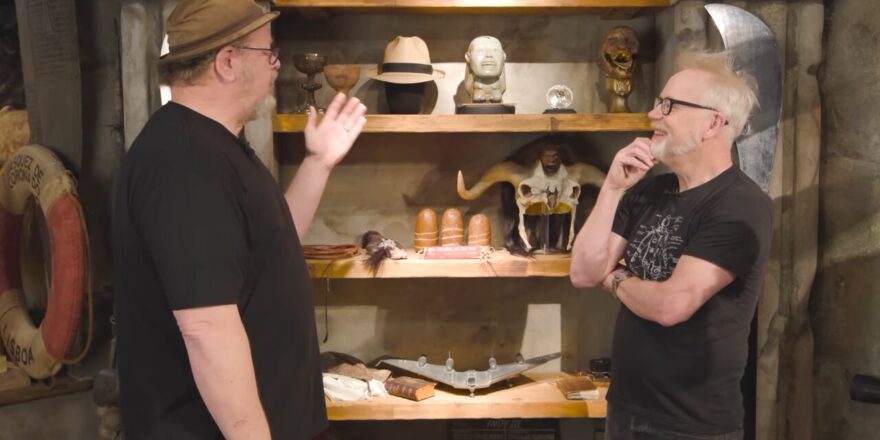 Two men in front of rustic shelves with movie props.