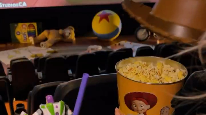 In the foreground, a popcorn bucket with a cowboy hat. In the background, items in front of a movie screen.