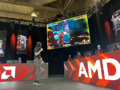 A man stands on a stage, looking at people play games on screen.